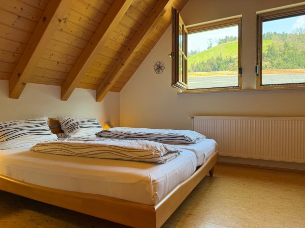 Ferienwohnung 4 Helles Schlafzimmer unter dem Dach mit zwei Betten und Fenstern zur Landschaft.